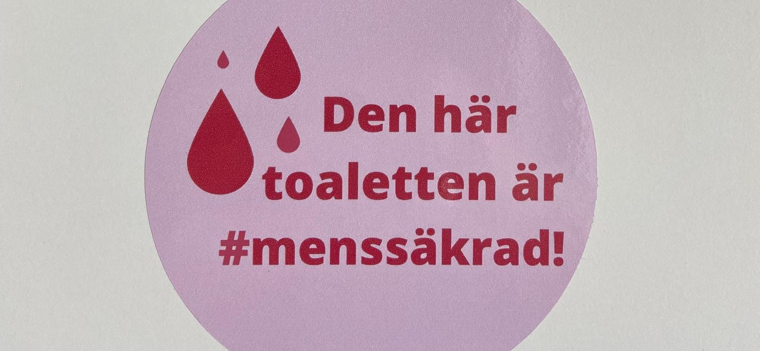 Ett klistermärke i rosa och med bloddroppar och texten "Den här toaletten är #menssäkrad!"