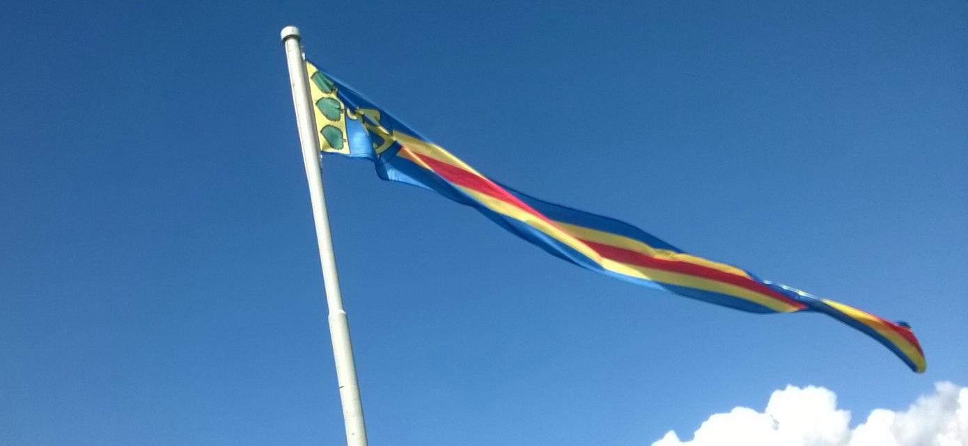 Åländsk vimpel mot blå himmel med stadens vapen