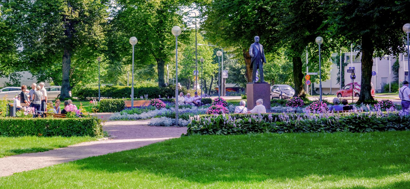 Statyn av Julius Sundblom med parkbänkar runt där människor sitter i sommarsolen