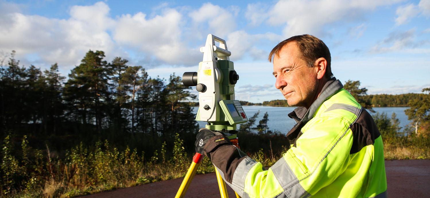 Man mäter tomt med hav i bakgrunden