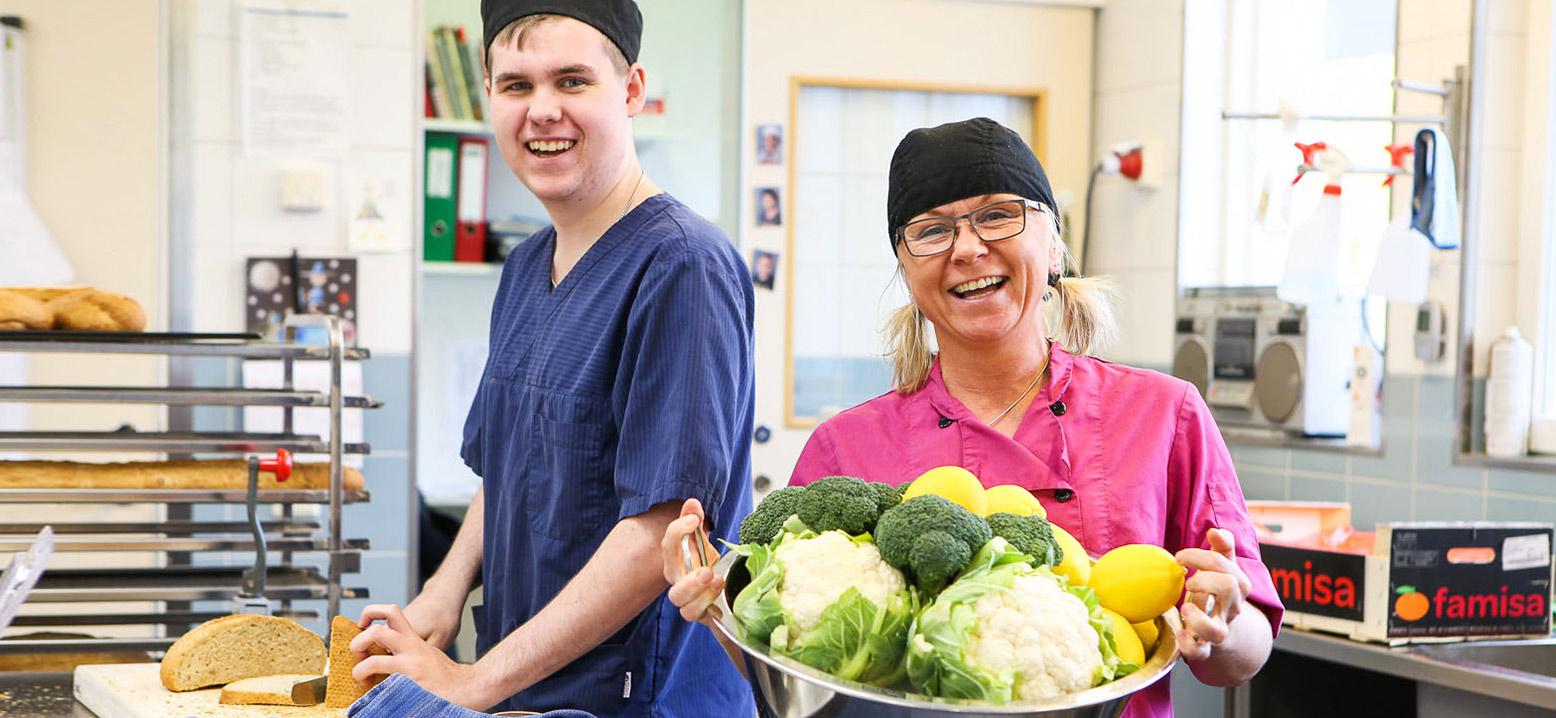 Bilden visar två personer i köket som håller fram grönsaker