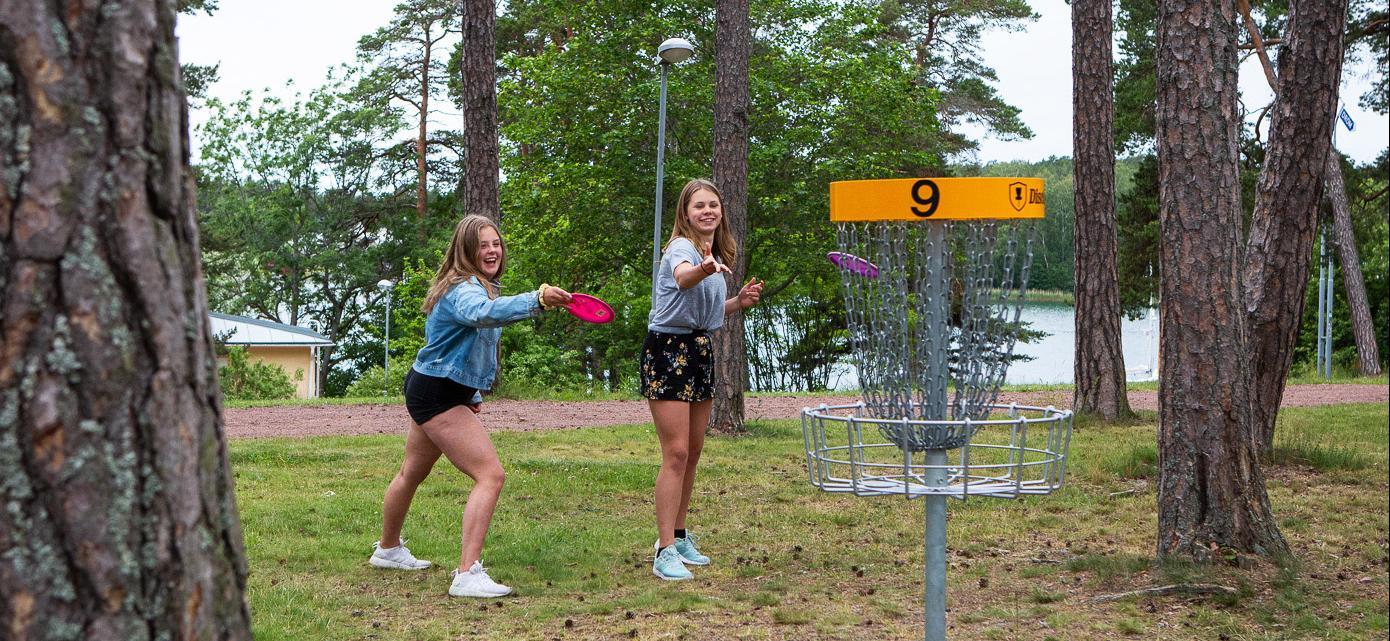 Två unga tjejer spelar discgolf och havets ses i bakgrunden