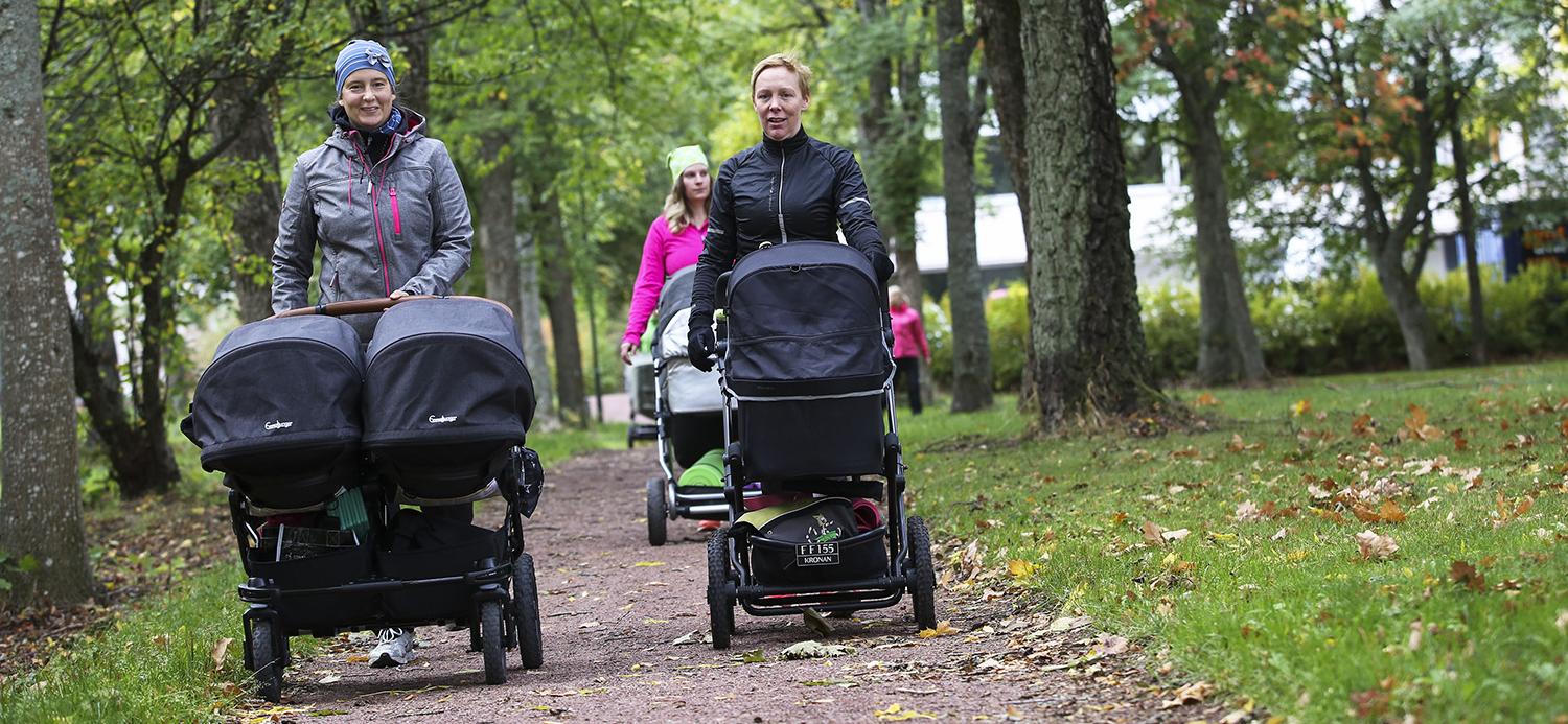 Bilden visar flera mammor med barnvagn som promenerar en höstdag.