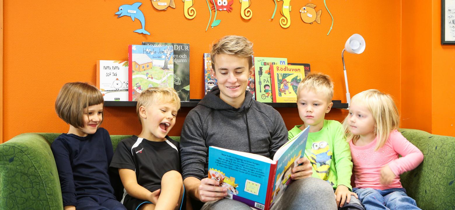 Bilden visar en manlig asssitent som läser saga för fyra barn