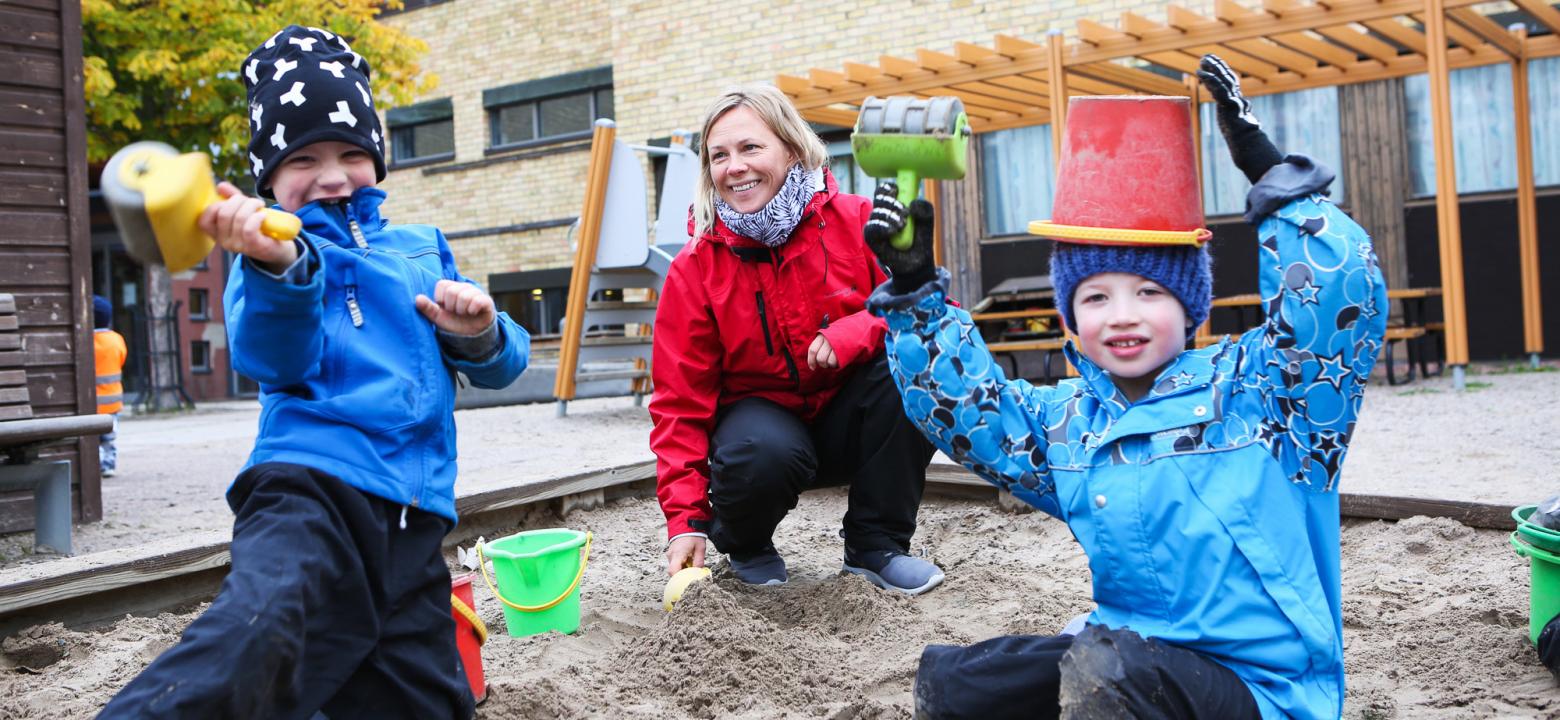 Bilden visar en anställd med två barn i sandlådan på Neptunus daghem, barnen skämtar och leker