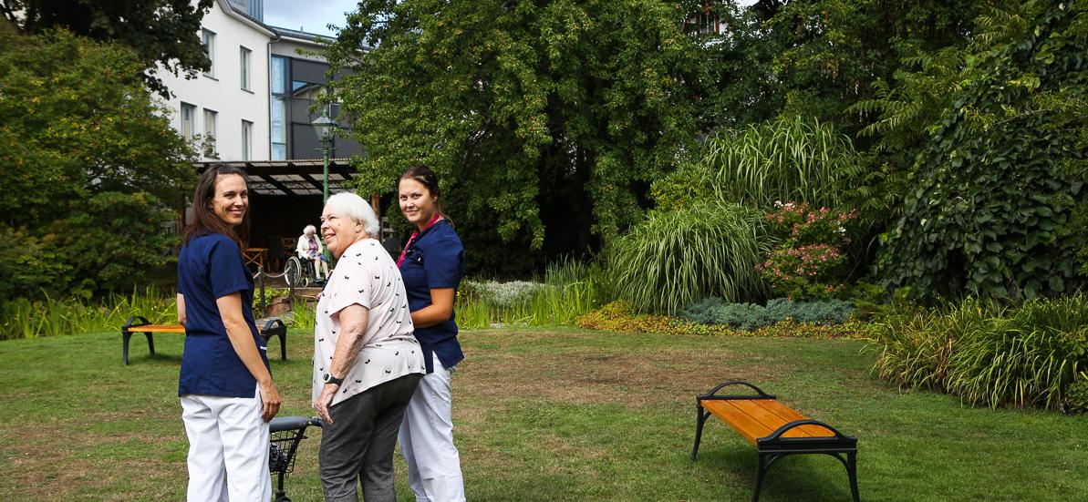 Två vårdare och en boende utomhus i en trädgård