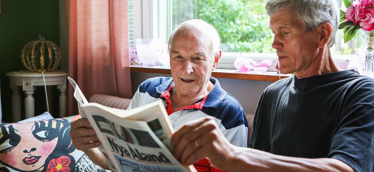 En hemserviceanställd läser tidning för en äldre man