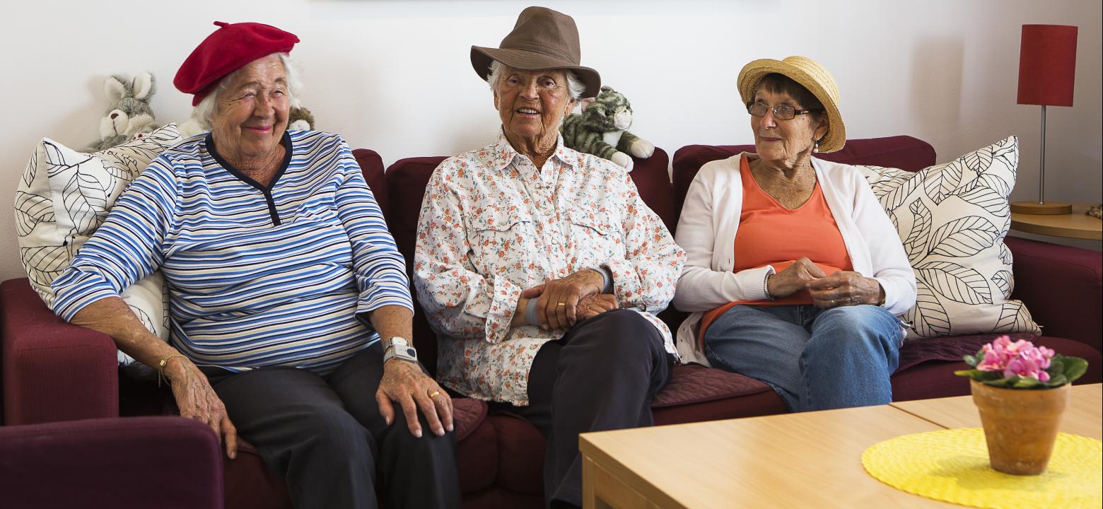 Tre glada damer i hattar sitter i Klippans soffa