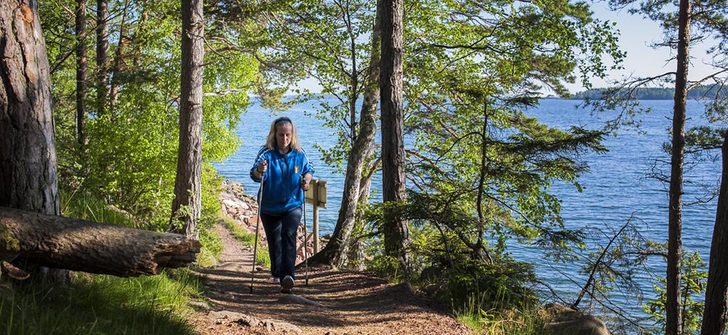 En kvinna promenerar med stavar längs en stig nära havet