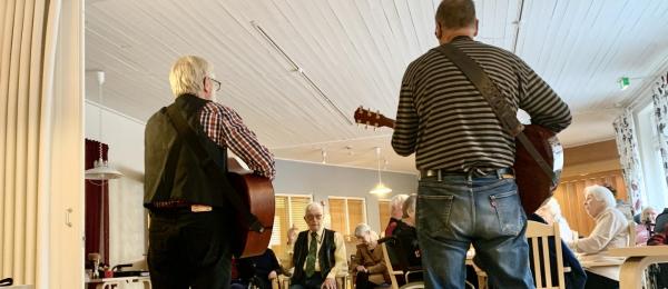 Två musiker med gitarrer spelar för äldre på stadens boende