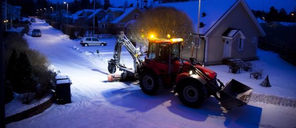 En traktorgrävare som plogar snö på en gata i staden.