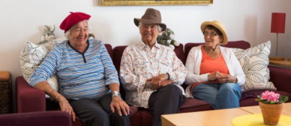 Bilden visar lite äldre personer som umgås sittande i en soffa