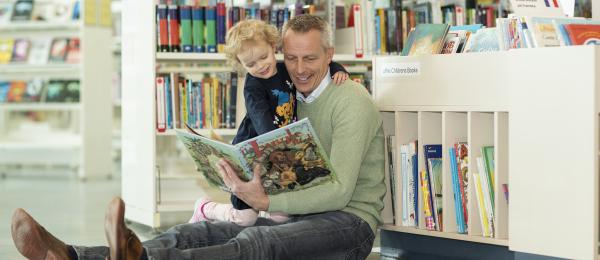En pappa läser för sitt barn i stadsbiblioteket