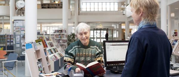 En äldre dam lånar en bok från bibliotekarien